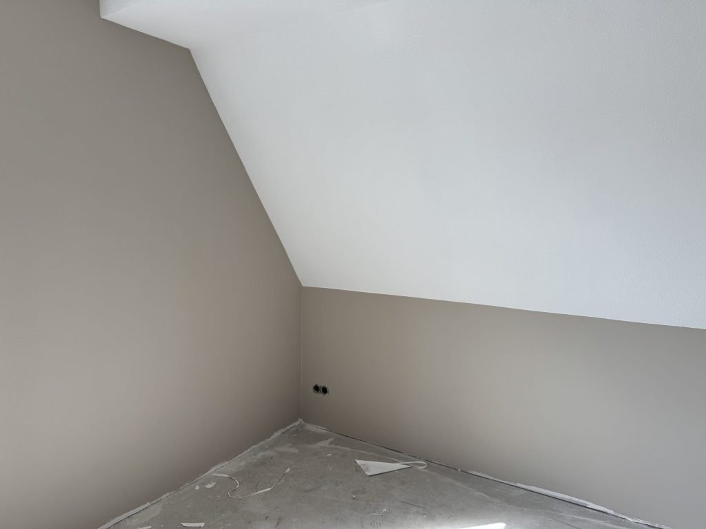 Zolderkamer met een schuine wand, de muren in een warme grijstint en het schuine vlak wit